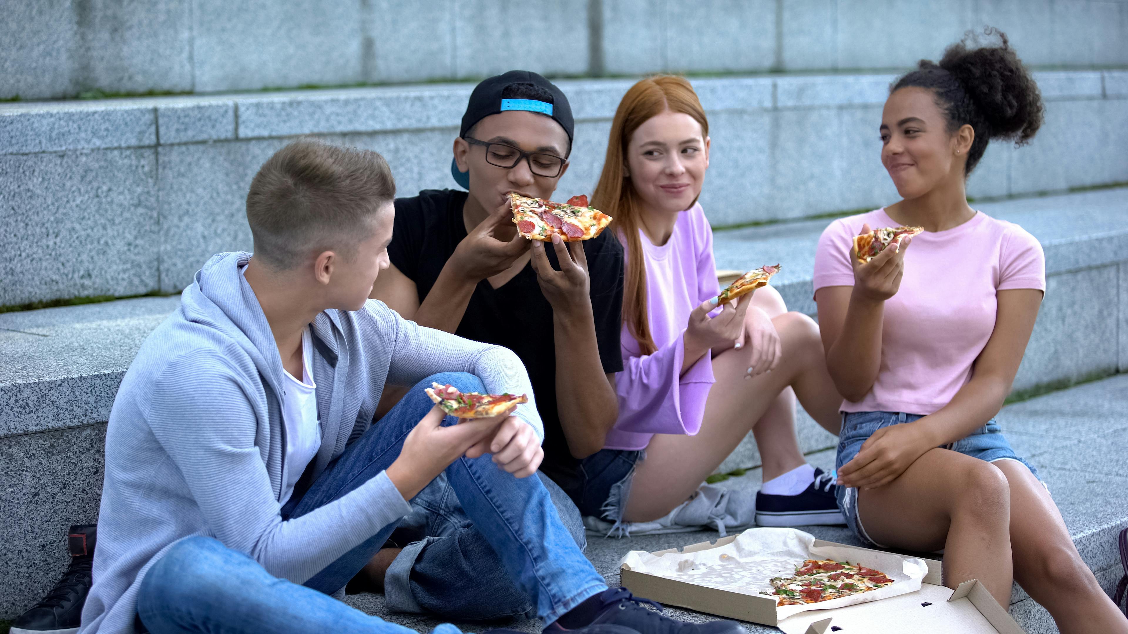 Teens eating pizza outside