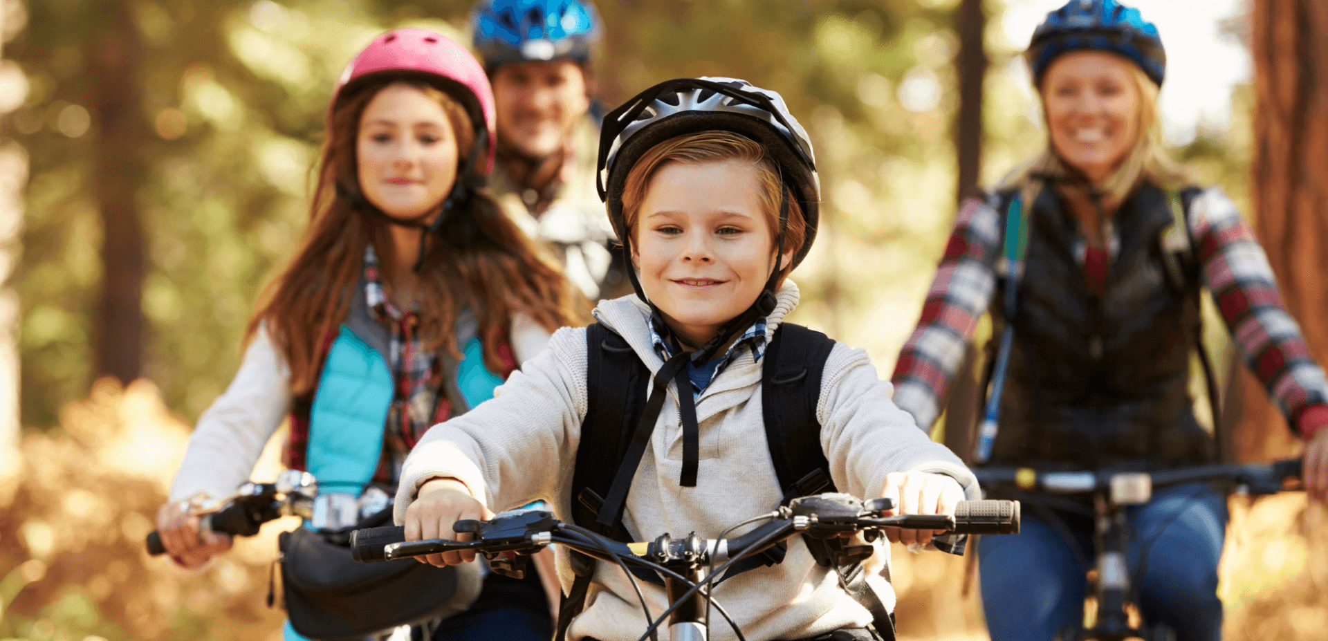Young boy, older girl, both parents in background riding bikes outside
